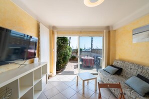 A living room with a TV, sofa, and a balcony with a table and chairs. - Le gîte du port - CANET-EN-ROUSSILLON (CANET-EN-ROUSSILLON)