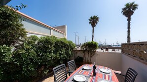 Un área de comedor al aire libre con una mesa preparada para cuatro personas, rodeada de sillas y palmeras al fondo.
