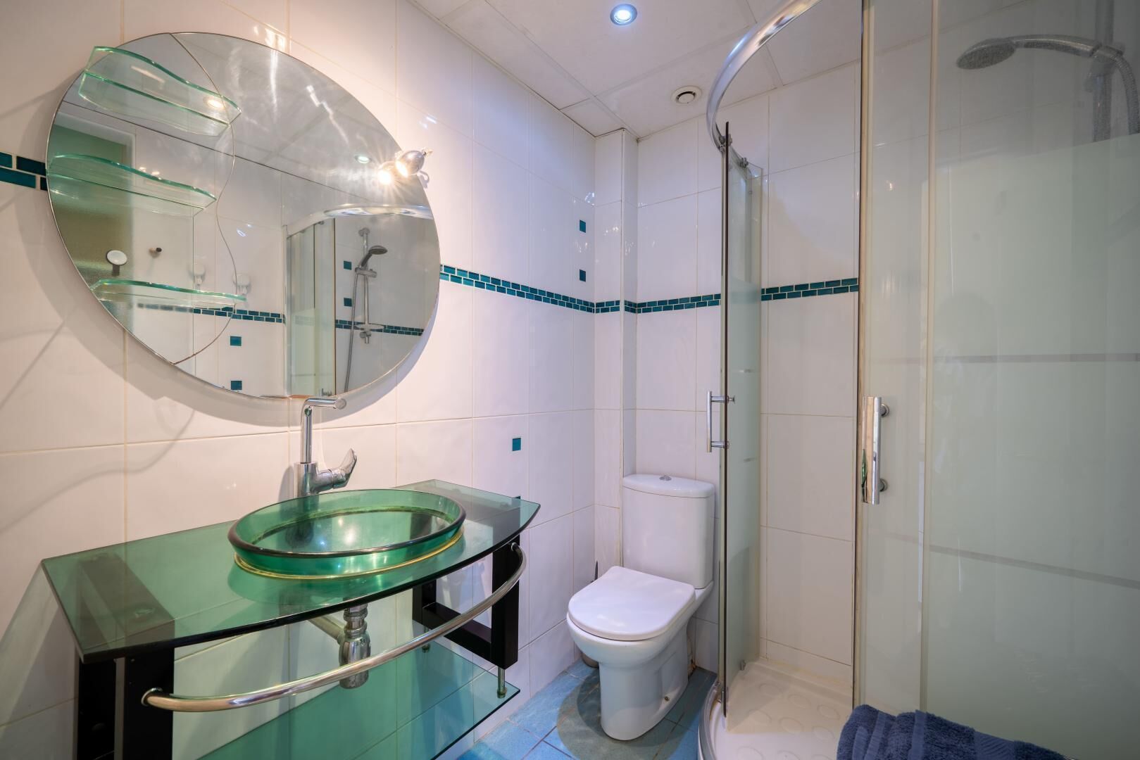 A modern bathroom with a glass sink, a toilet, and a glass-enclosed shower.
