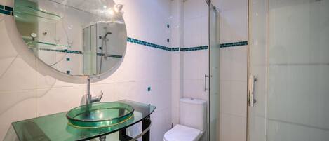 A modern bathroom with a glass sink, a toilet, and a glass-enclosed shower.