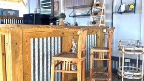 A wooden bar area with two chairs, a small shelf with decorative items, and a television mounted on the wall. - Cozy 2-Bedroom Retreat in Cabo Rojo Near the Beach (Cabo Rojo)