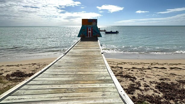 A wooden pier leading to a beach with a boat in the water and a colorful structure labeled 'EL COMBAT'. - Cozy 2-Bedroom Retreat in Cabo Rojo Near the Beach (Cabo Rojo)