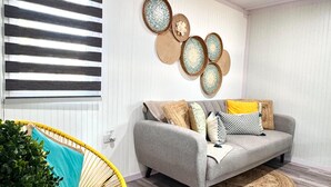 A living room with a grey sofa, yellow chair, woven rugs, and wall decor. - Cozy 2-Bedroom Retreat in Cabo Rojo Near the Beach (Cabo Rojo)