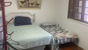 Ein Schlafzimmer mit zwei Betten, einem Deckenventilator, einem Fenster mit Gitter und einem Bild an der Wand.