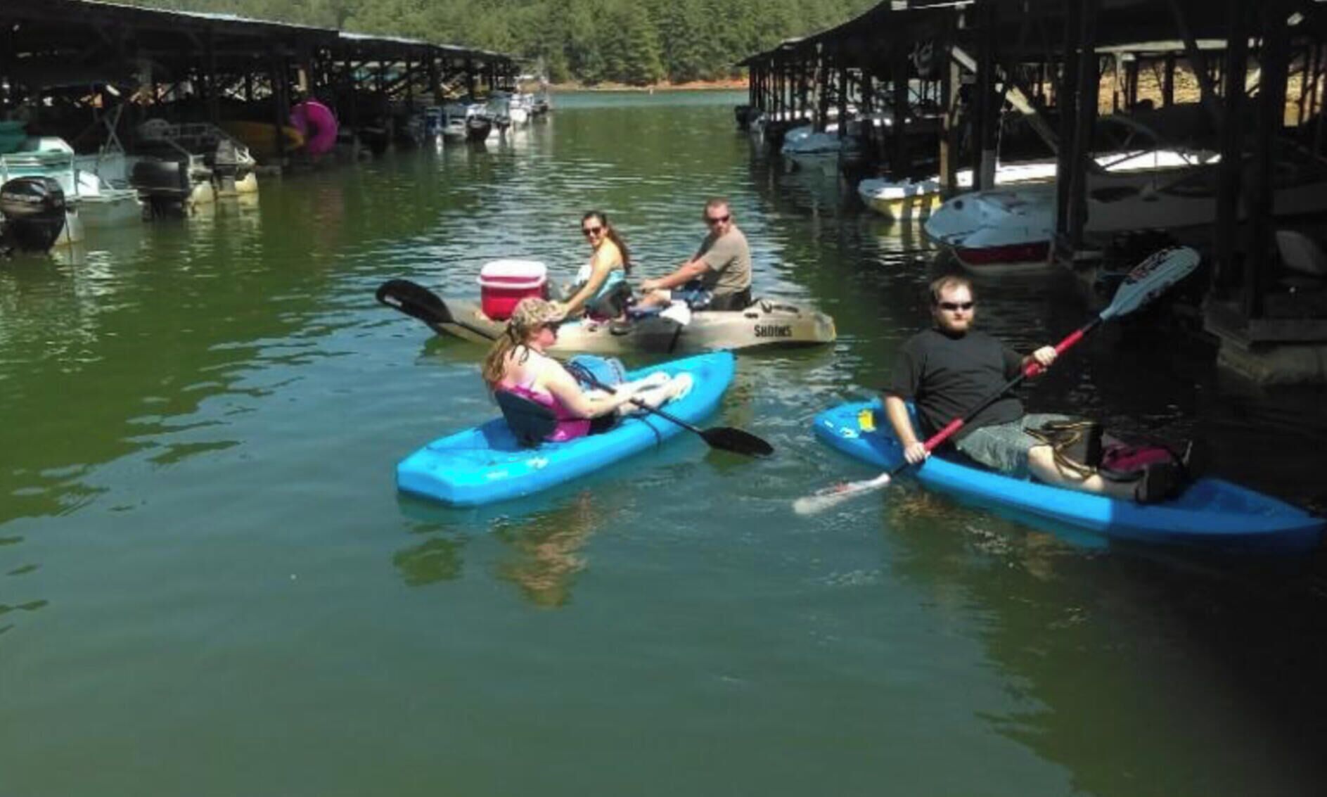 A group of people kayaking on a calm river with boats docked on the sides.