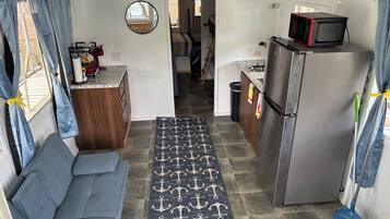A compact kitchen with a refrigerator, microwave, and a small dining area with a bench.