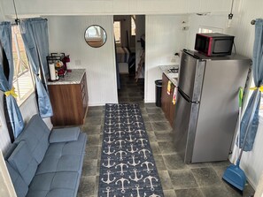 A compact kitchen with a refrigerator, microwave, and a small dining area with a bench. -  Peaceful , nature-focused mountain escape, Relax at 'Gunny’s Anchor Murphy, NC. (Murphy)