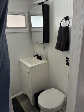 A small, white bathroom with a white sink, a mirror, a towel rack, and a toilet.