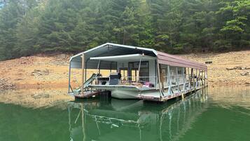 A floating houseboat with a covered deck and a small dock.