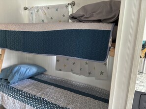 A bunk bed with a patterned bedspread, a pillow, and a curtain with star patterns.