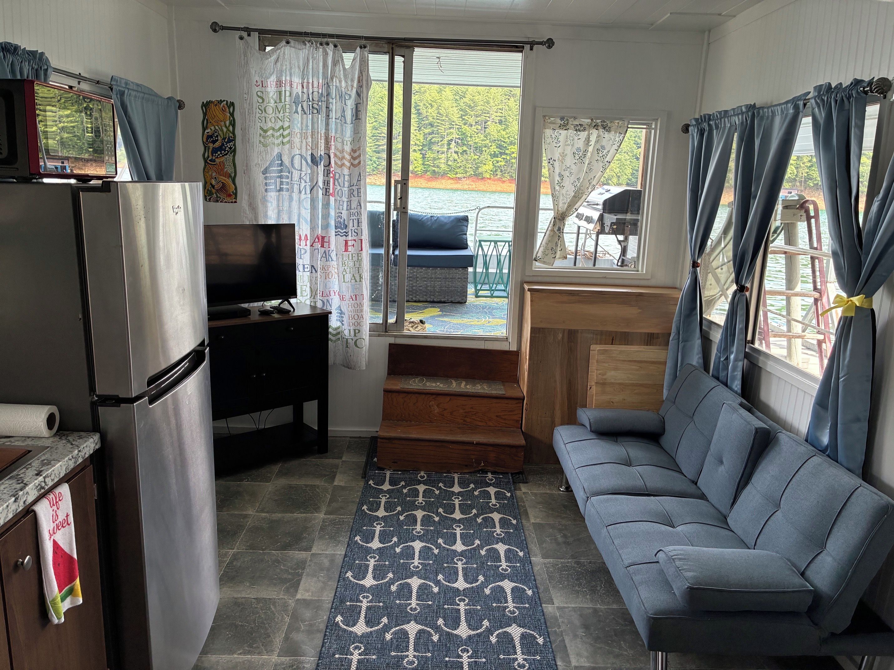 Un espacio habitable compacto con kitchenette, un sofá, una televisión y vista a un muelle y al agua.