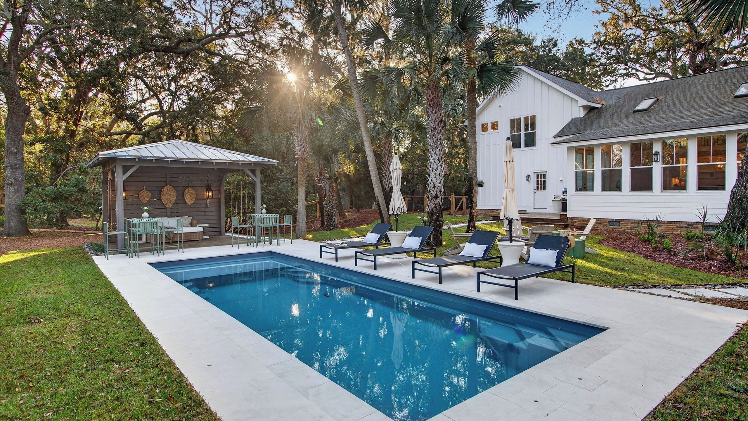 Une piscine avec des chaises longues, un espace de détente couvert et une maison en arrière-plan.