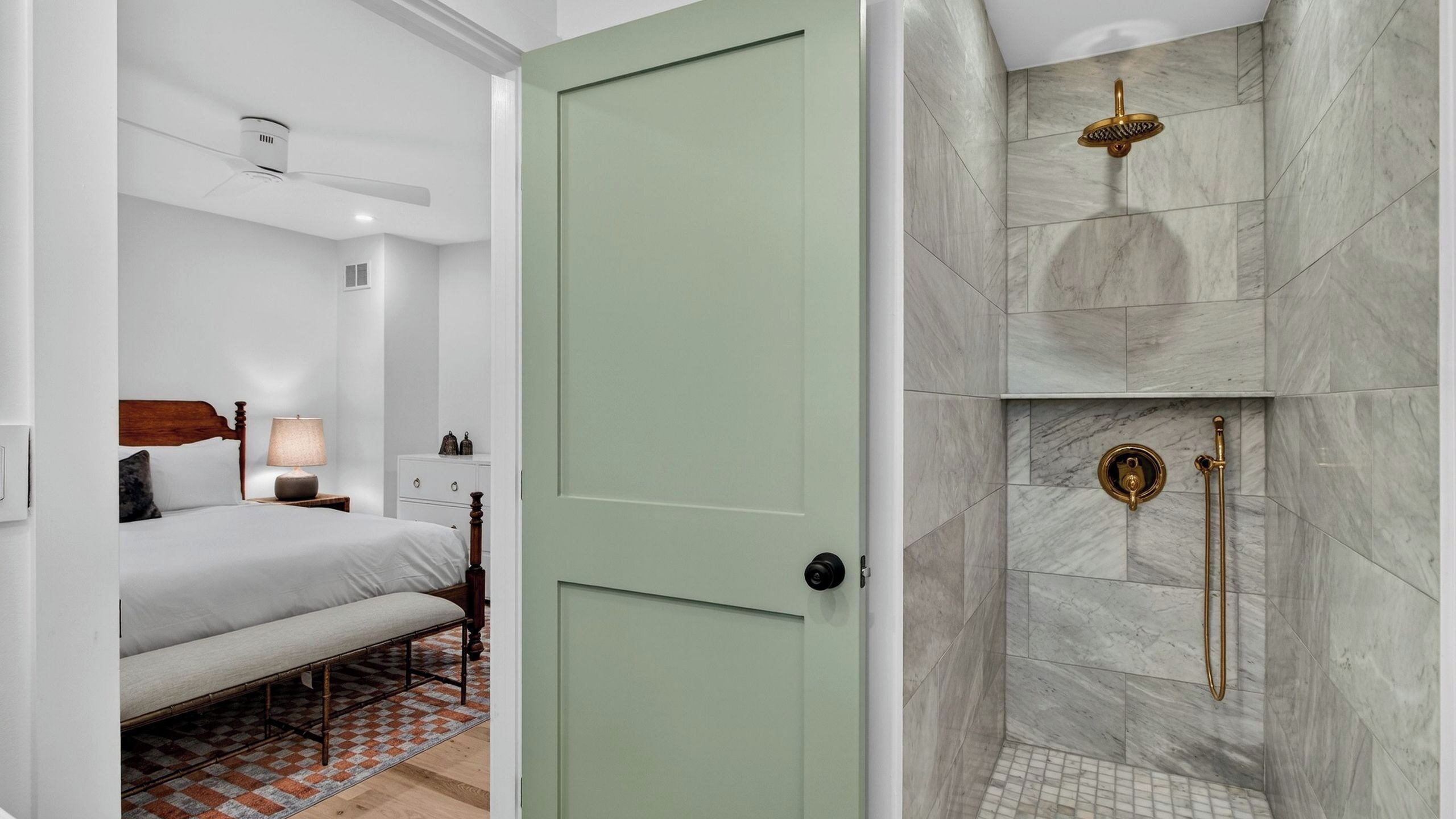 A bedroom with a bed, bedside table, lamp, and a bathroom with a shower and marble tiles.