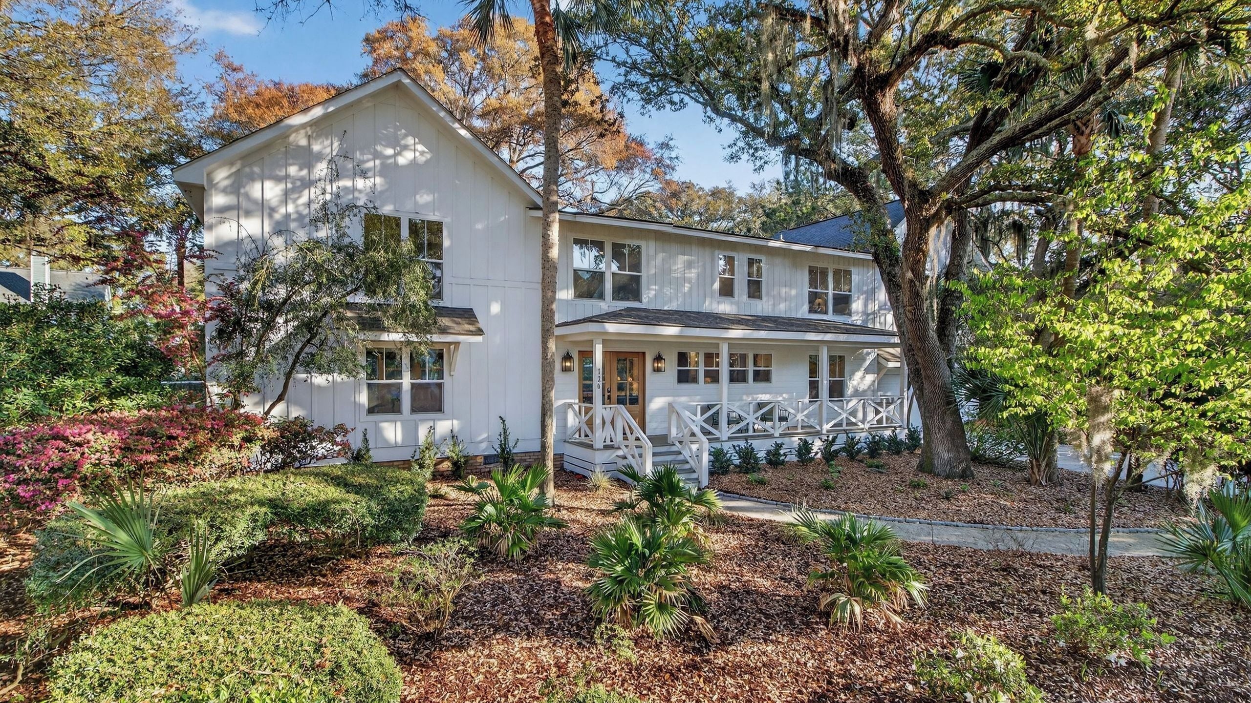A two-story house with a porch, surrounded by landscaped garden beds and trees.