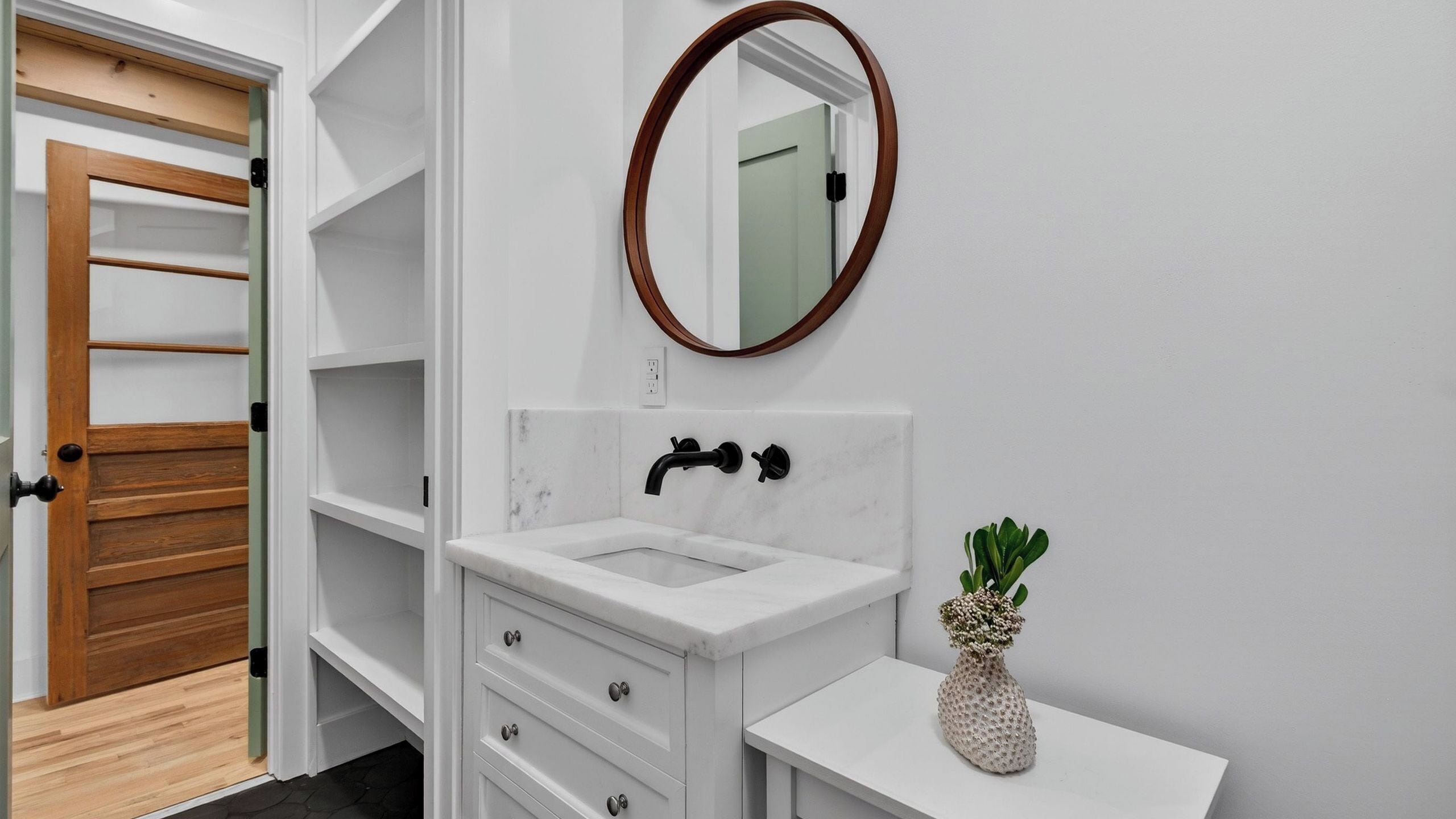 A bathroom with a white vanity, a wooden door, a marble sink, and a mirror.