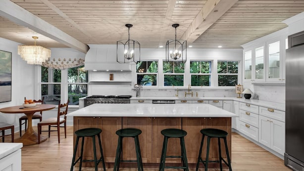 Een moderne keuken met een groot schiereiland, barstoelen, houten balken en grote ramen.