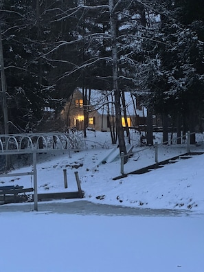 Schneebedeckte Landschaft mit einem Holzhaus und einem Metallzaun.