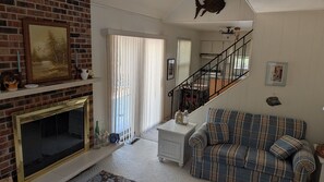 Ein Wohnzimmer mit Kamin, einem karierten Sofa, einer Treppe und einer Küche im Hintergrund.