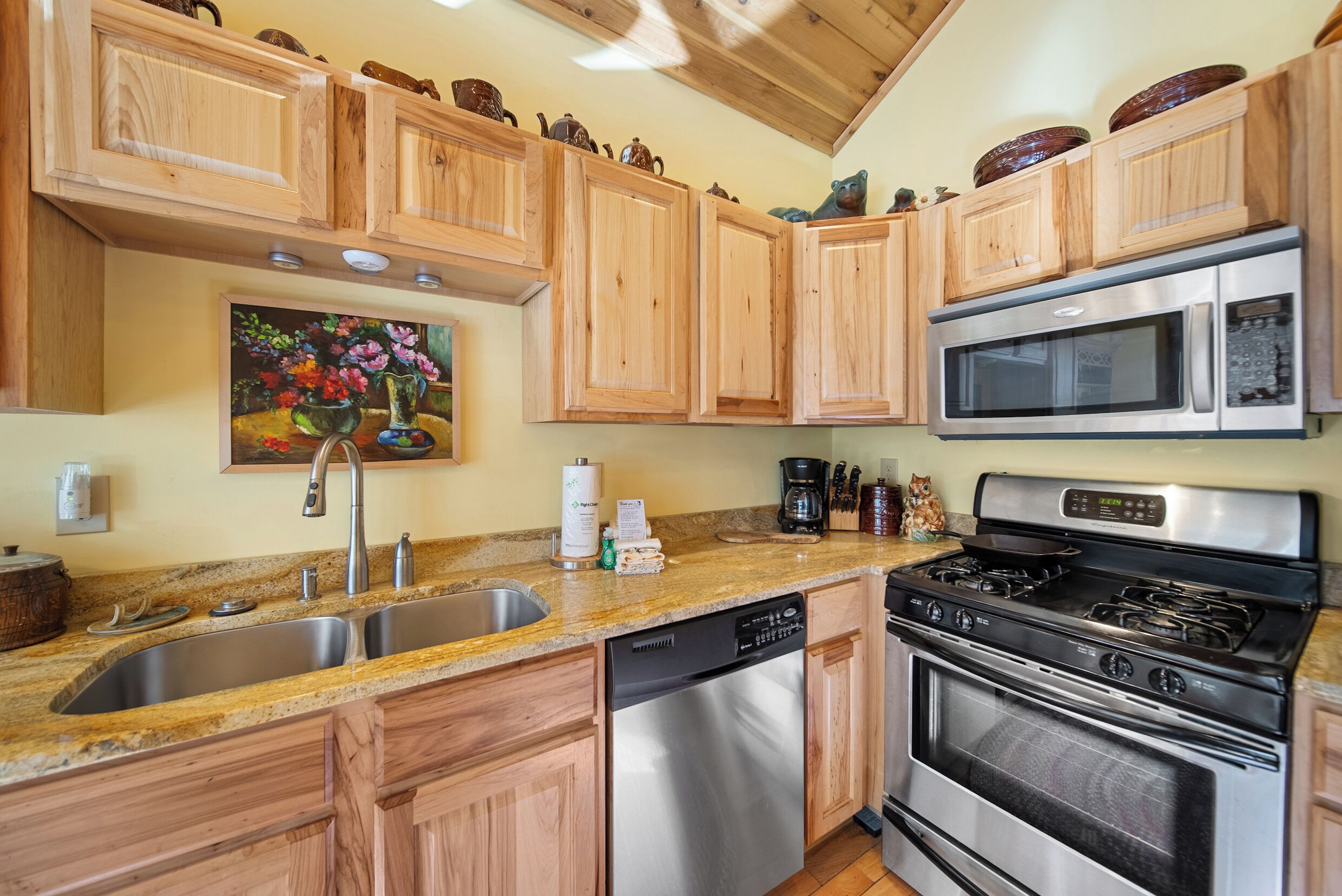 A kitchen with wooden cabinets, stainless steel appliances, a double sink, and a painting on the wall.