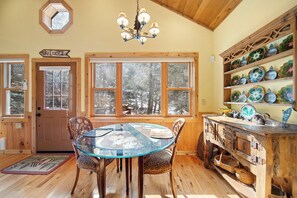 A wooden interior with a glass table, chairs, a chandelier, and a shelf with decorative plates. - Charming Beech Mtn Retreat Near Slopes | Cozy Fireplace Escape (Banner Elk)