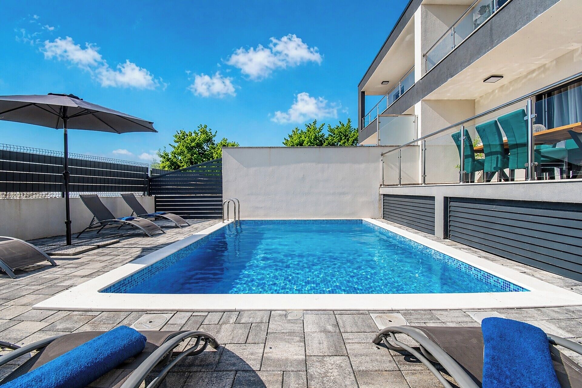 A swimming pool with lounge chairs and an umbrella, surrounded by a modern building.