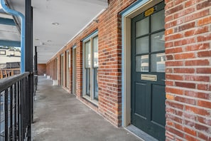 A corridor with brick walls and large windows, leading to a door marked with the number 208.