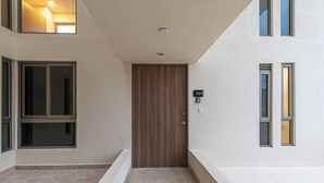 Ein schmaler Korridor mit einer Holztür, einem kleinen Fenster und einer Leuchte.