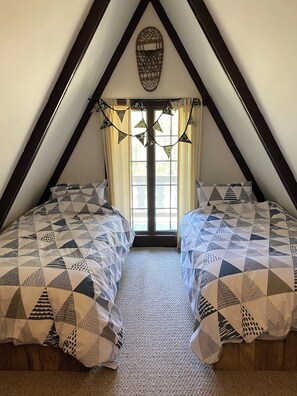 Ein Schlafzimmer mit zwei Betten, einer geneigten Decke und einem Fenster mit Vorhängen.