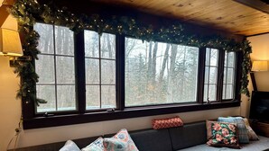 Une pièce chaleureuse avec une grande fenêtre, un canapé agrémenté de coussins à motifs et un téléviseur posé sur un meuble en bois.