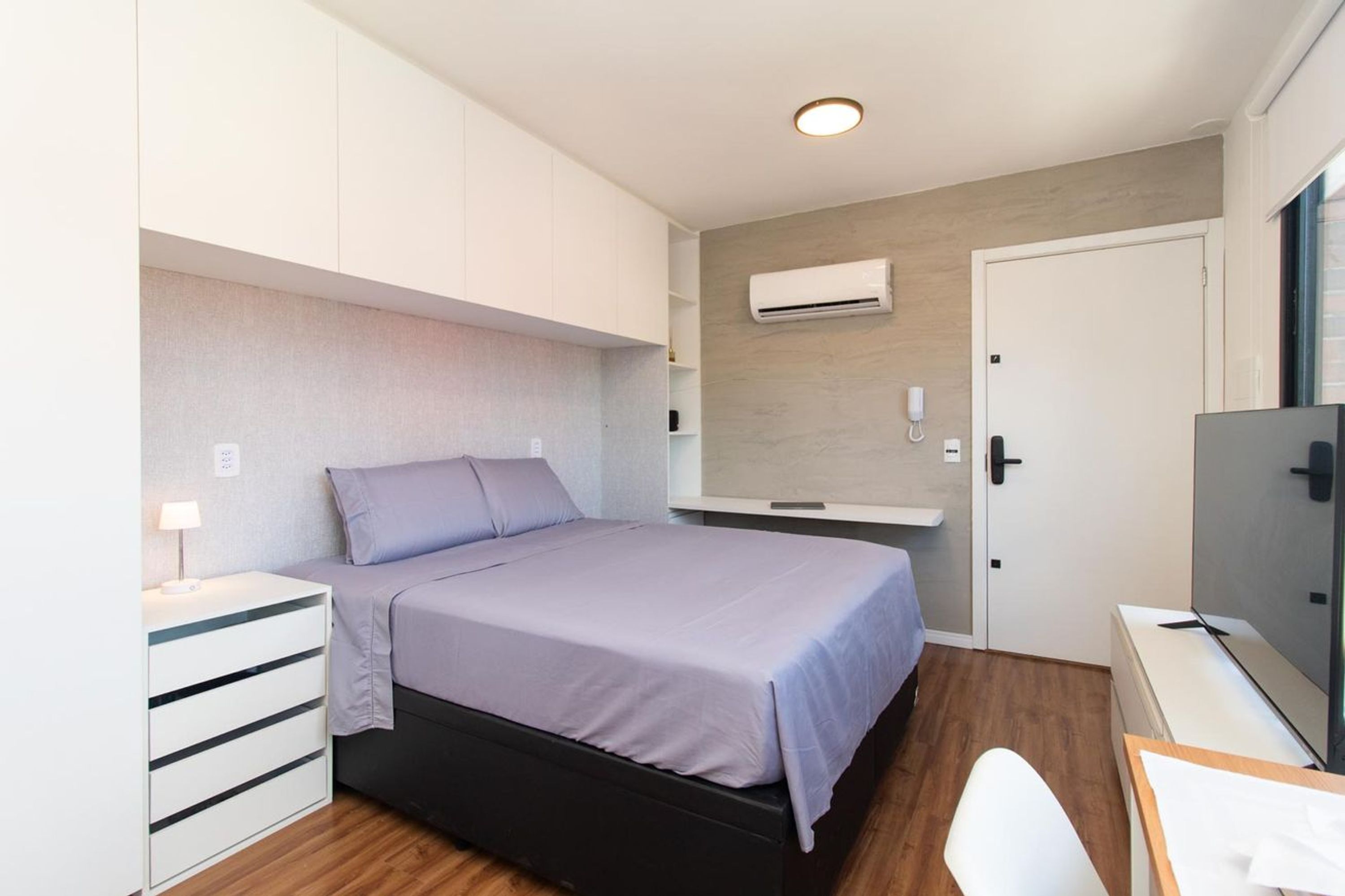 Een slaapkamer met een bed, een bureau, een stoel, een kledingkast, een airconditioning en een deur.