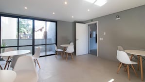 A modern interior with large windows, white tables, and chairs. - Studio c Vaga Smart Lock e Ar no Vila Jo o Pessoa (Porto Alegre)