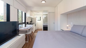 A modern hotel room with a large bed, a desk with a chair, a television, and a view of the outdoors. - Studio c Vaga Smart Lock e Ar no Vila Jo o Pessoa (Porto Alegre)