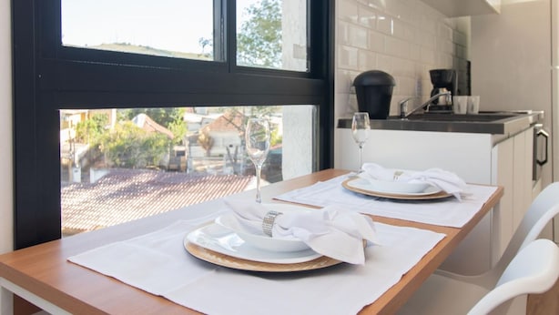 A dining table set with plates and napkins, a wine glass, and a coffee maker in the background. - Studio c Vaga Smart Lock e Ar no Vila Jo o Pessoa (Porto Alegre)