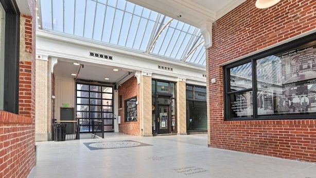 A spacious atrium with a high ceiling and skylight, featuring a brick wall and a glass storefront. - Local Discounts!-The Historic Newark Arcade (Newark)