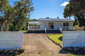 A two-story house with a covered porch, a front door, and a small front yard. - Blackpool Living – Beaches, Village & Easy Living (Waiheke Island)