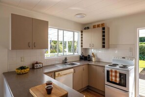 A modern kitchen with a built-in oven, a sink, and a window with a view of greenery. - Blackpool Living – Beaches, Village & Easy Living (Waiheke Island)
