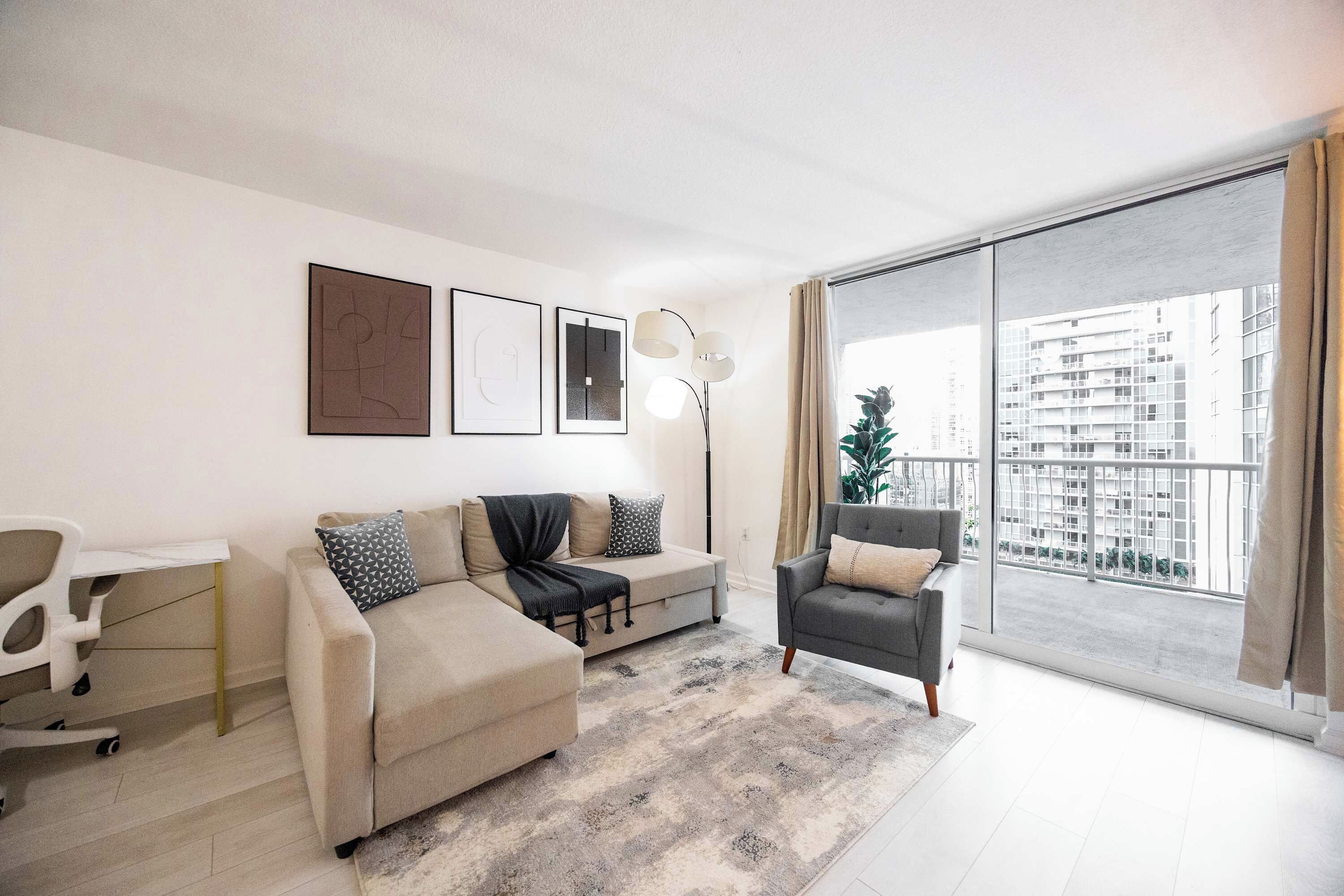 Ein modernes Wohnzimmer mit einer Couch, einem Sessel und einem großen Fenster mit Blick auf Gebäude.