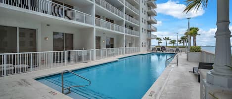 A multi-story hotel with a swimming pool, balconies, and a view of the sea.