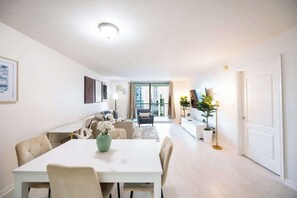 Ein modernes Wohnzimmer mit Essbereich, einer Sofagarnitur, einem Couchtisch mit einer Vase und Blick durch eine Glastür.