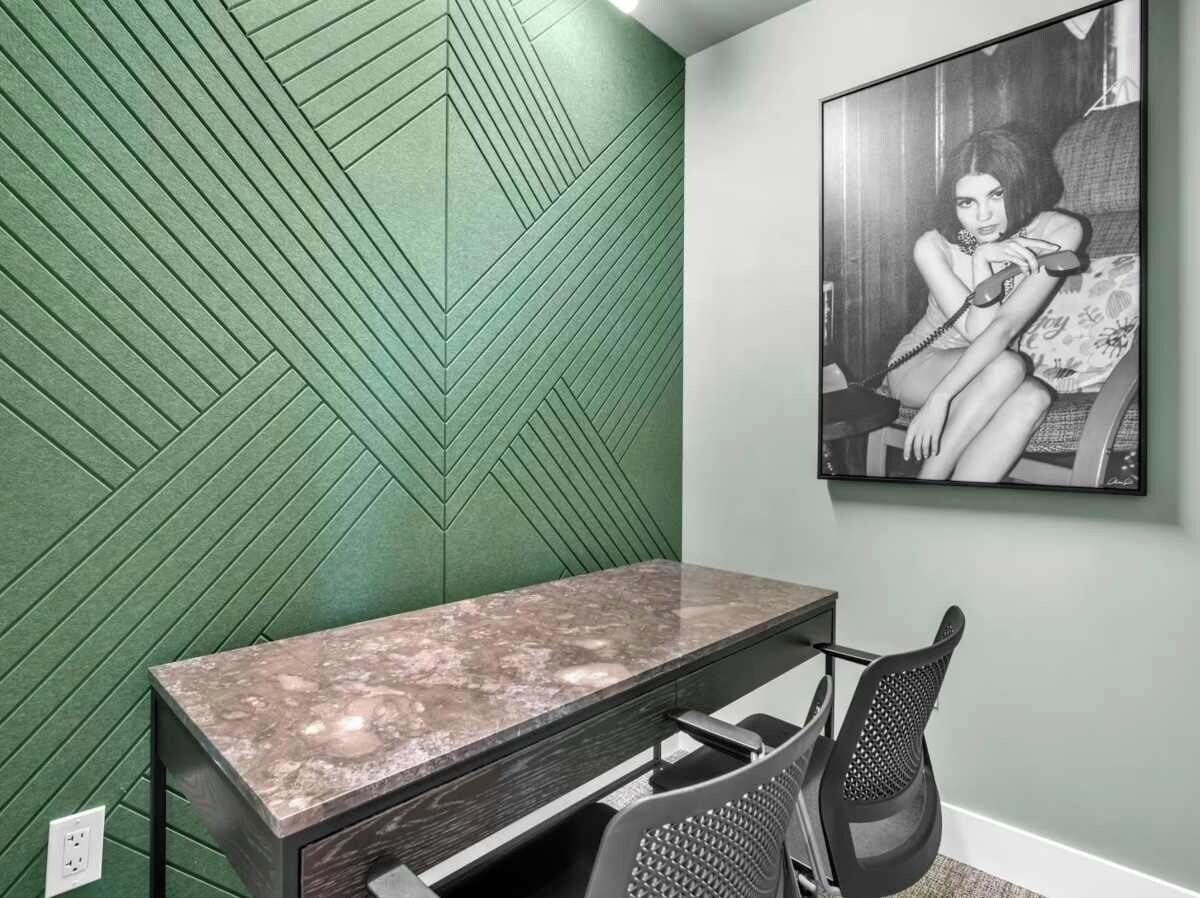 Een kamer met een groen gestructureerde wand, een bureau met een marmeren blad, een zwarte bureaustoel en een zwart-wit foto in een lijst aan de muur.
