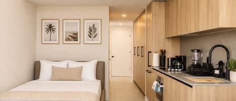 A modern hotel room with a bed, a kitchenette, and a bathroom.