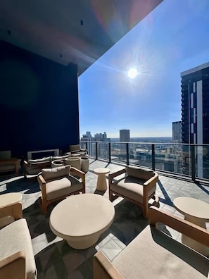 A rooftop terrace with outdoor seating, a clear view of the city skyline, and a modern building with a visible sign. - Luxurious New Studio | Rooftop Pool & Prime Area (Miami)