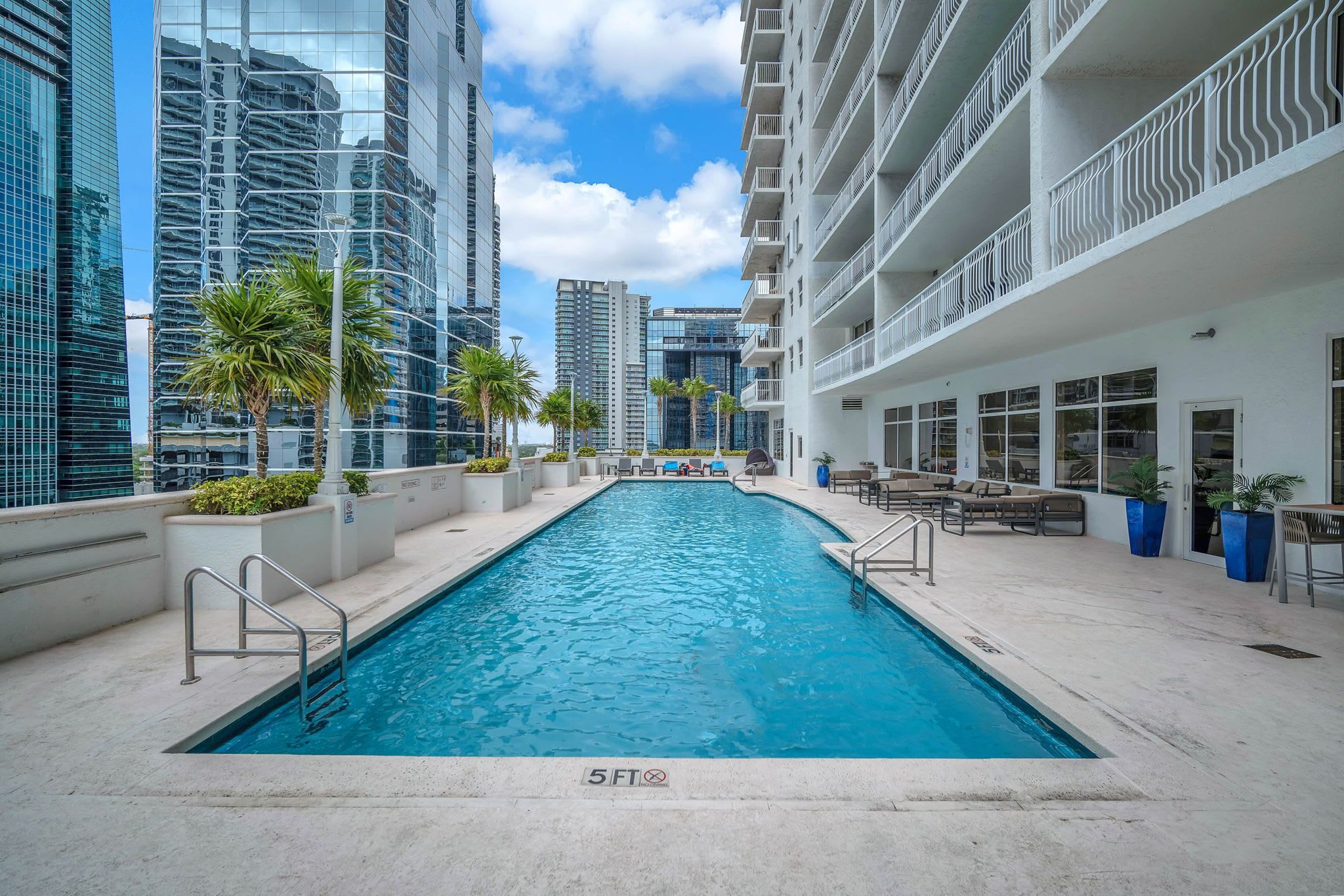 Une piscine entourée de bâtiments modernes, sous un ciel dégagé.