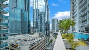 A high-rise building with a glass facade, a rooftop parking area, and a pool area with palm trees. - Stylish Brickell 1BR - Free Parking - Sleeps 6 (Miami)