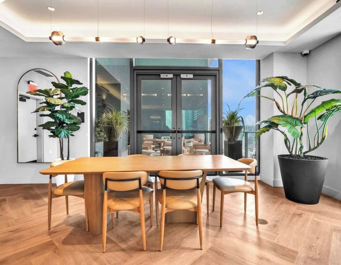 Une salle de conférence moderne, dotée d’une grande table en bois, de six chaises et de plantes en pot.