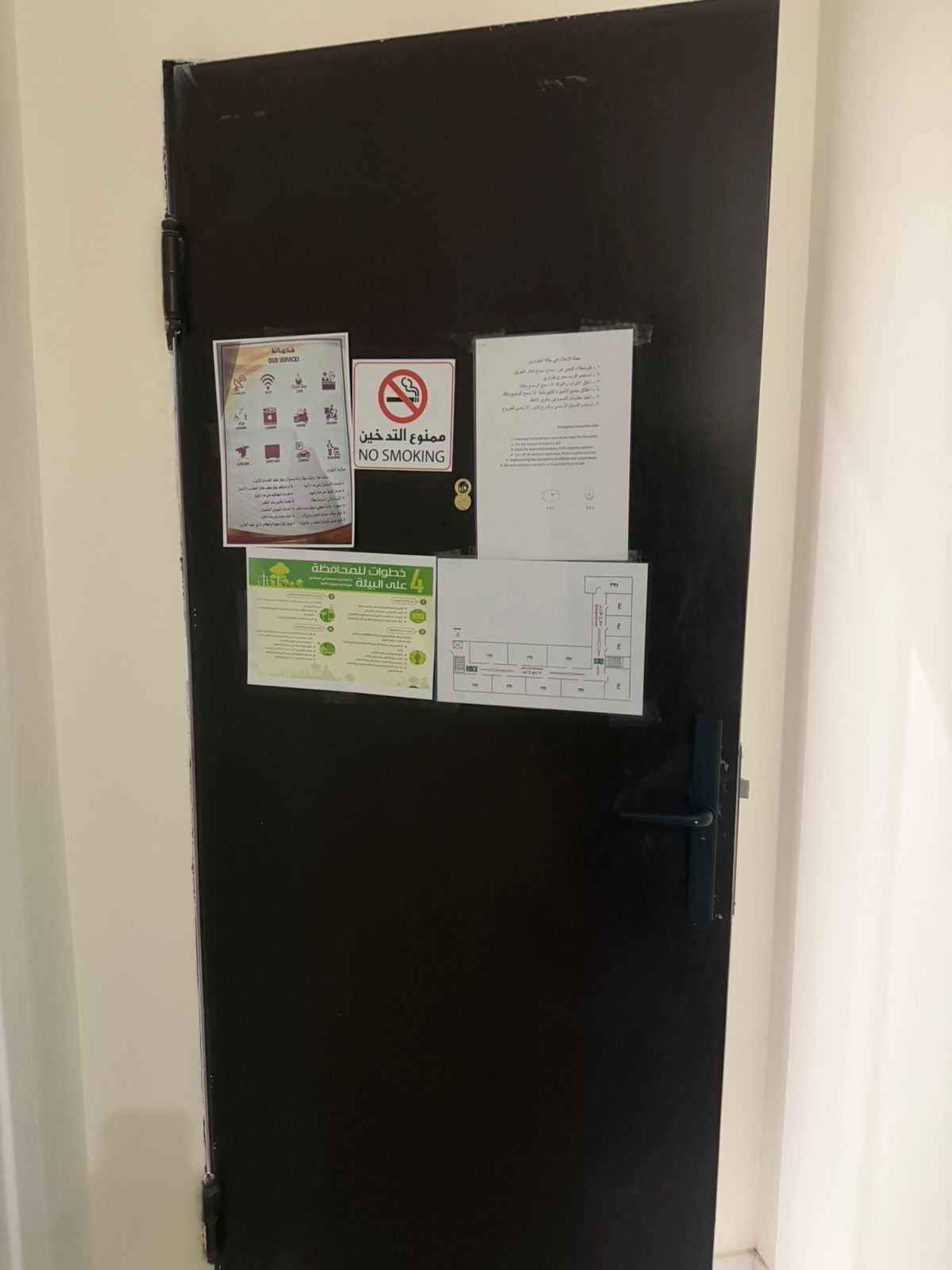 Une porte sur laquelle sont affichées plusieurs informations, notamment un panneau interdisant de fumer, une feuille d’information sur les services offerts et une feuille d’information générale.