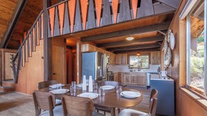Un interior de madera con una mesa de comedor dispuesta para cuatro, una cocina con armarios de madera y una escalera con barandillas de madera.