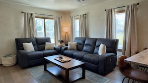 A living room with a dark leather sofa set, a wooden coffee table, and a dining table with chairs. - Hackberry Haven | Pet-friendly | Great Yard (Fredericksburg)