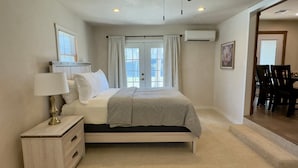 A bedroom with a bed, bedside table, lamp, air conditioning unit, and a view through a door. - Hackberry Haven | Pet-friendly | Great Yard (Fredericksburg)