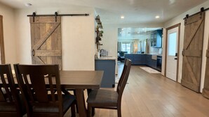 A dining area with a wooden table and chairs, a kitchen with blue cabinets, and a sliding barn-style door. - Hackberry Haven | Pet-friendly | Great Yard (Fredericksburg)